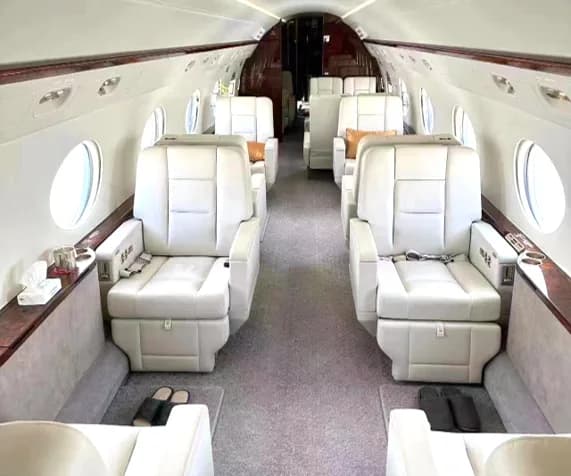 The luxurious interior of a private jet cabin with white leather seats and polished wood accents.