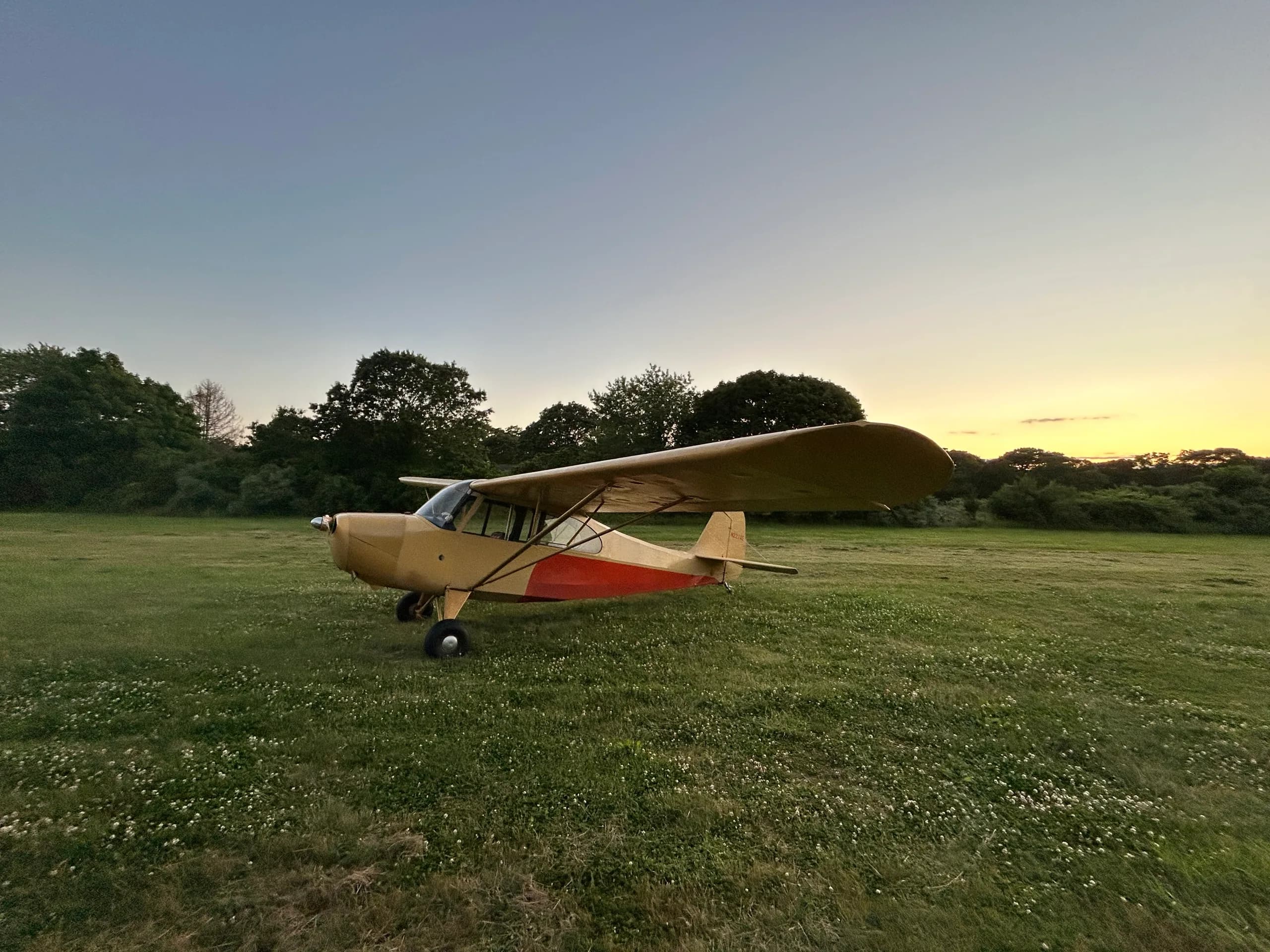 A yellow and orange Aeronca 7AC Champ aircraft parked on a grassy field at sunset.