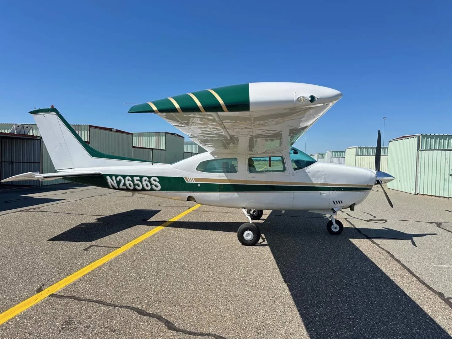 A white and green Cessna Centurion N2656S parked on an airfield under a clear blue sky.
