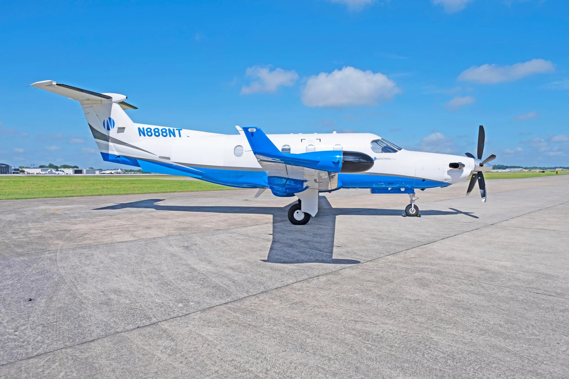 A white and blue Pilatus PC-12 aircraft, tail number N888NT, parked on a tarmac with a clear blue sky.
