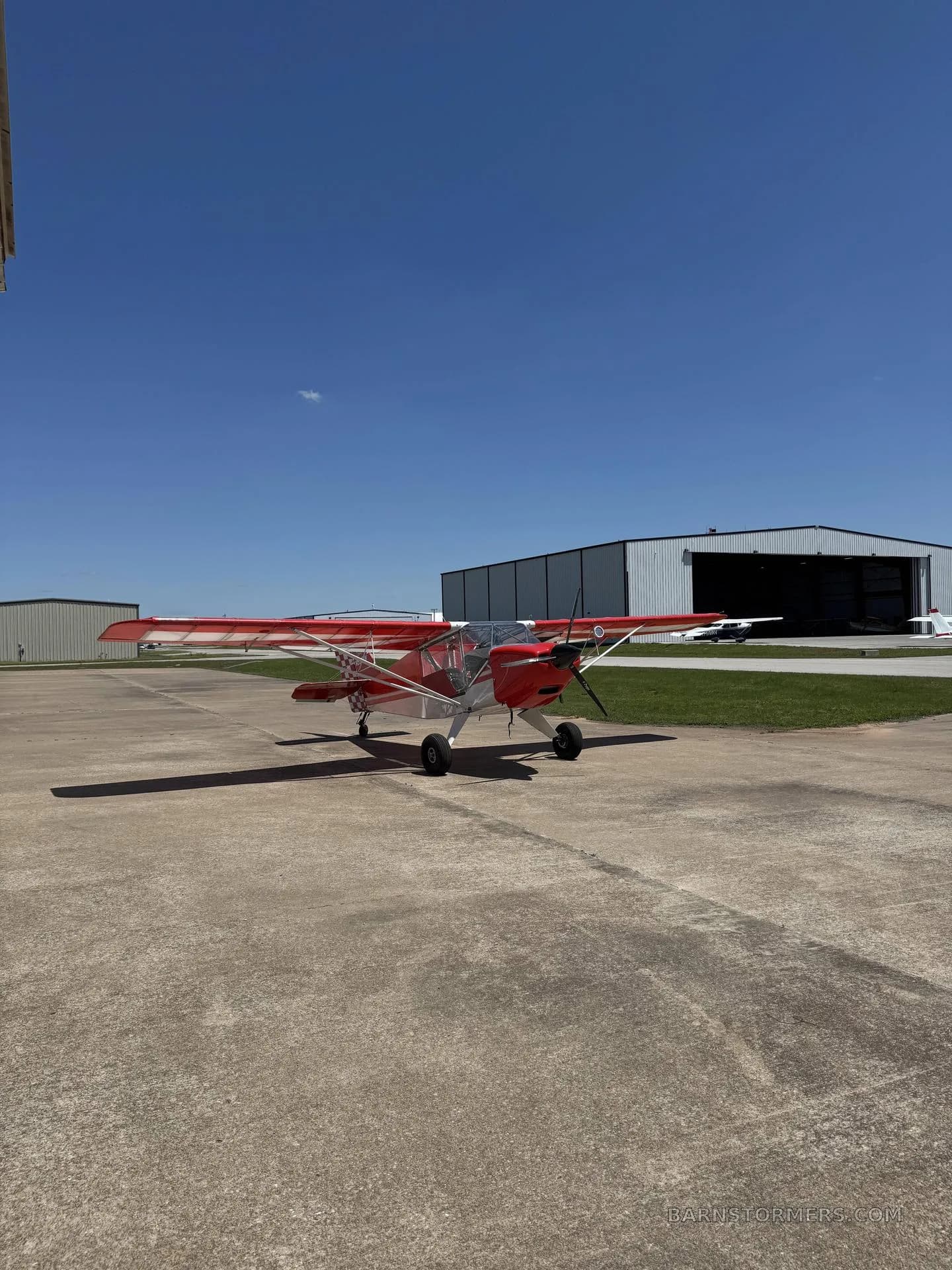 A red light sport aircraft with white accents parked on an airport tarmac under a clear blue sky.