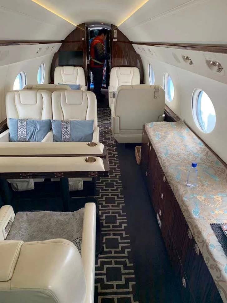 Interior view of the aircraft cabin with cream-colored leather seats, a table, and a patterned carpet.