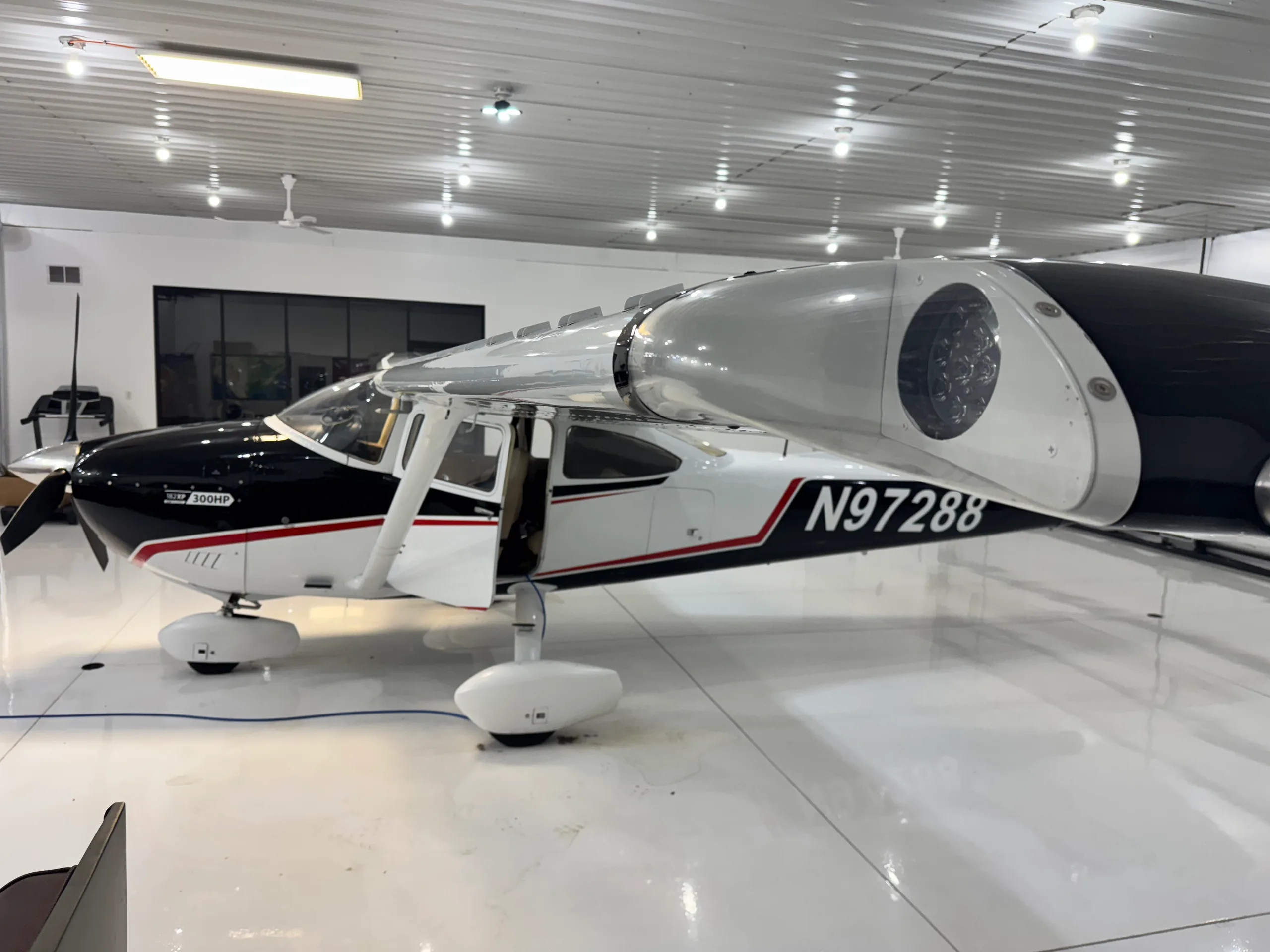 A full right-side view of a black and white Cessna 182XP aircraft with registration N97288, parked in a hangar with its door open.
