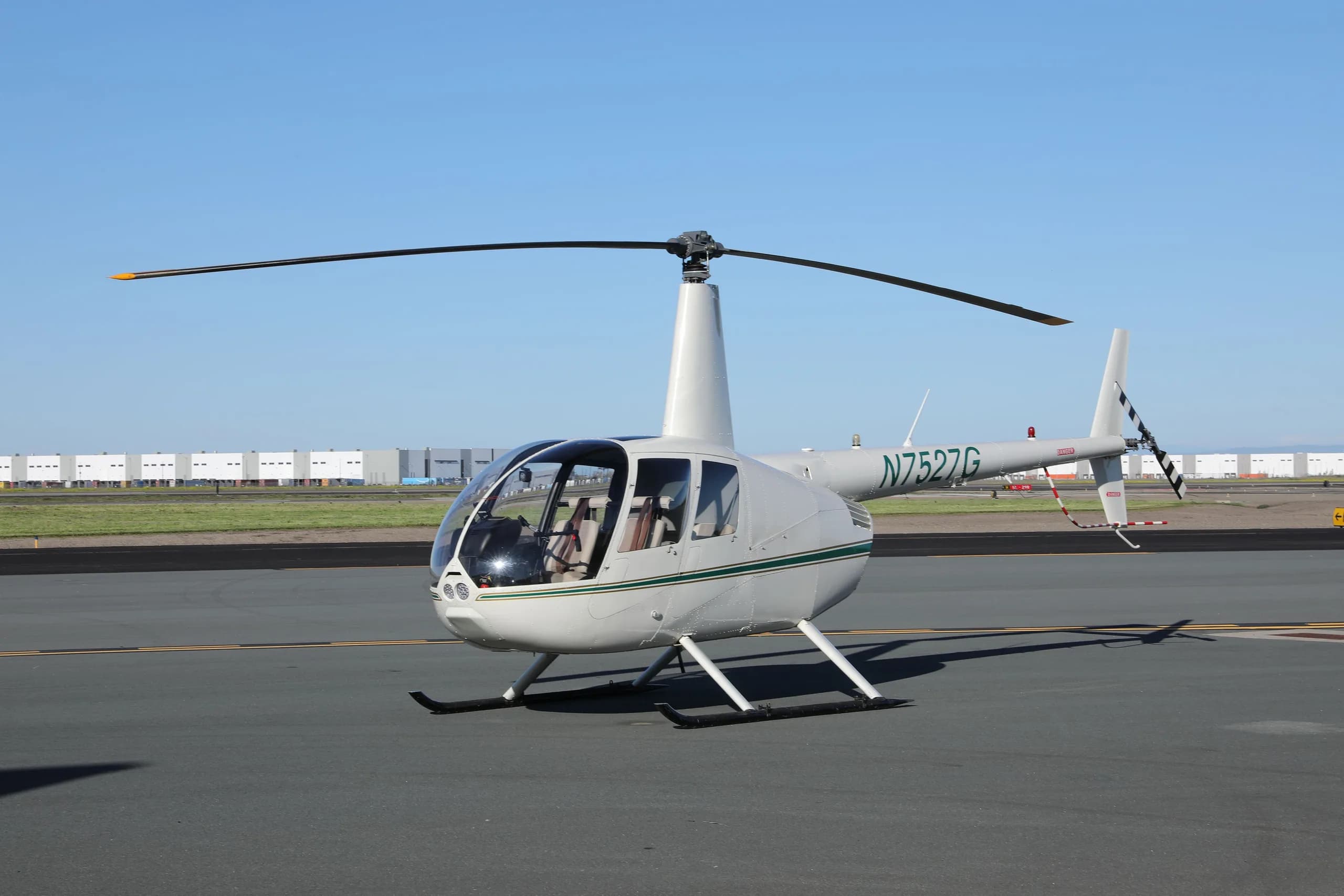 White Robinson R44 Raven II helicopter with a green stripe, registration N7527G, parked on an airfield.