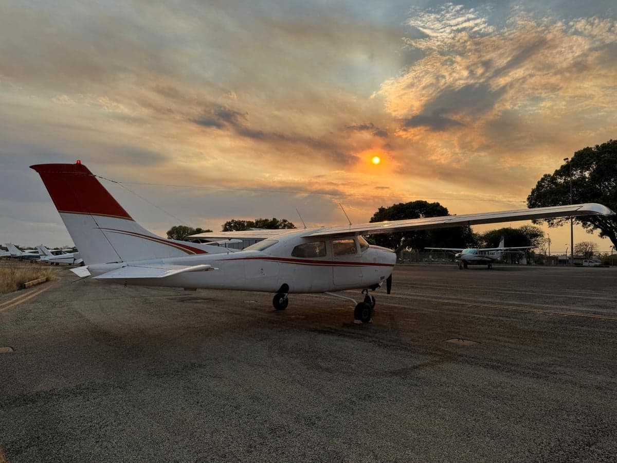 A Cessna 210 Centurion aircraft parked on the tarmac at sunset.