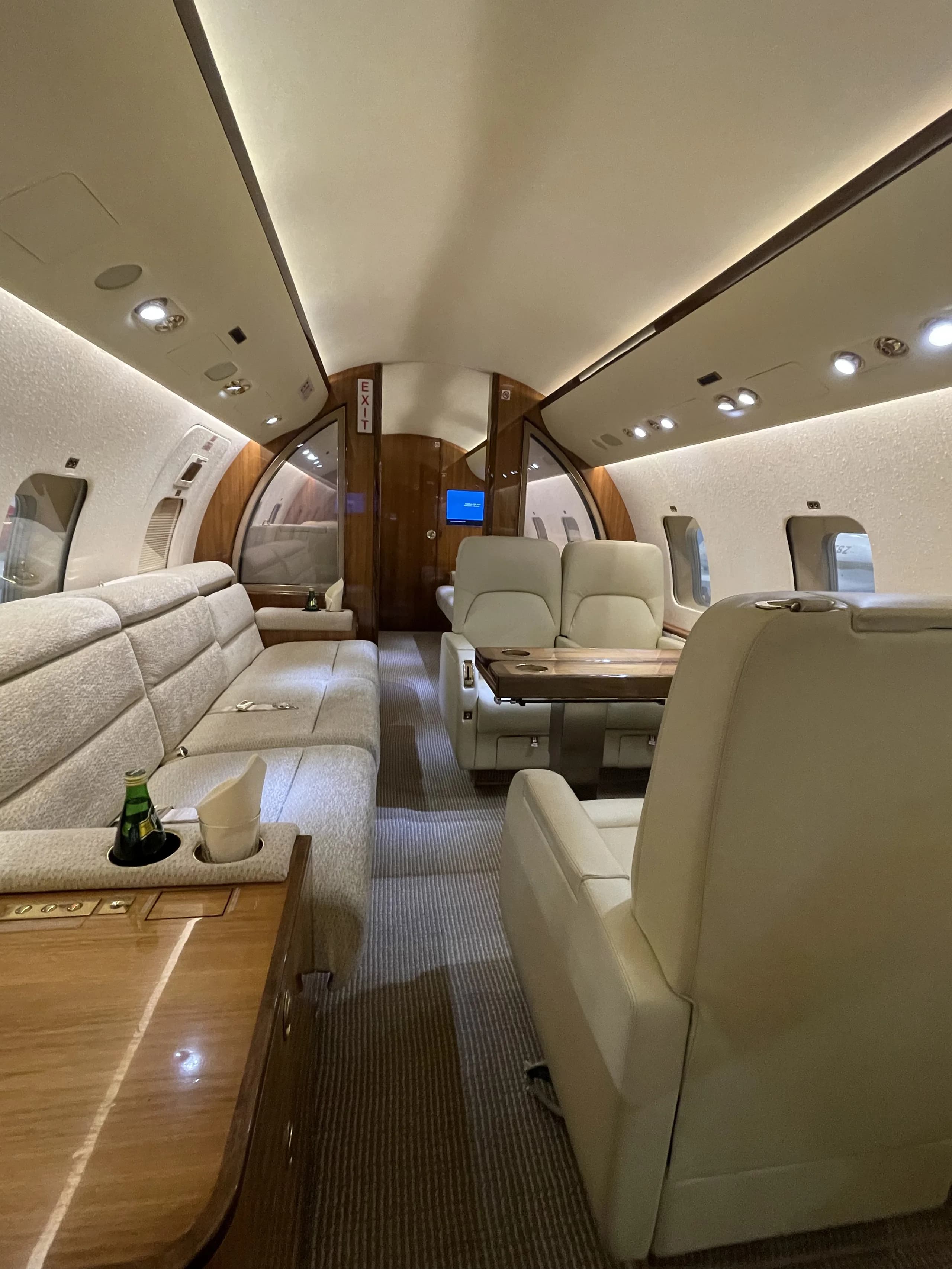 A spacious private jet cabin featuring a comfortable sofa, individual seats, and wooden tables.