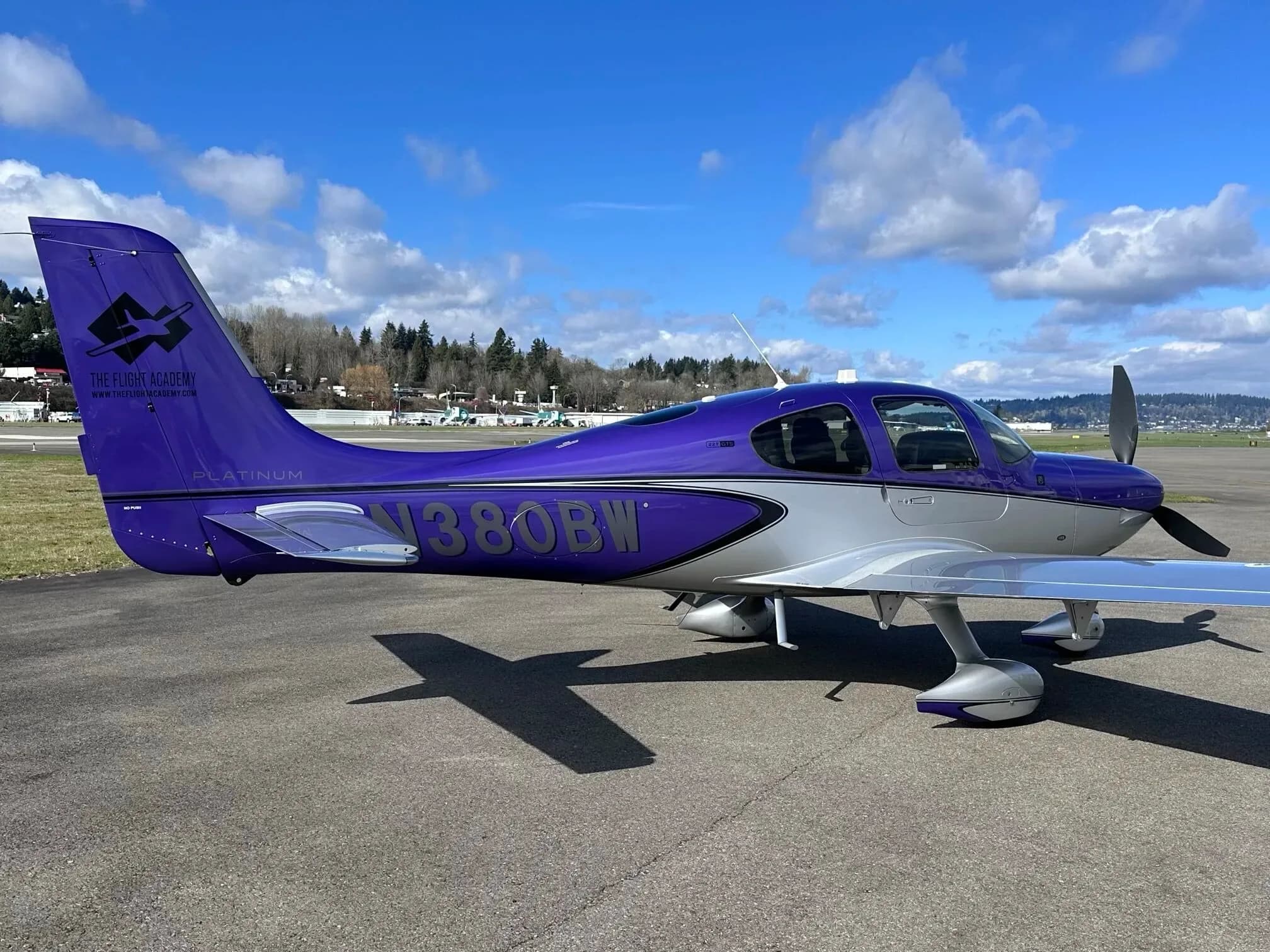 A three-quarter rear view of the purple and silver Cirrus SR22 aircraft, N380BW, parked on an airport tarmac.