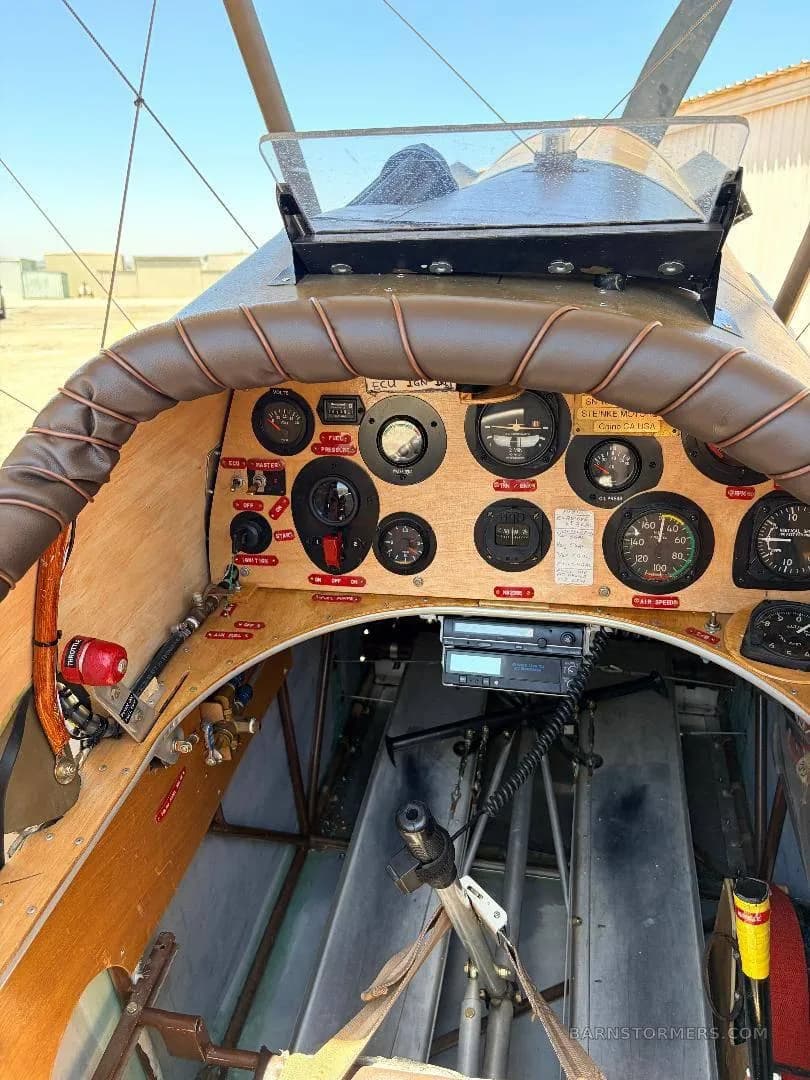 A close-up view of a vintage-style aircraft cockpit with a wooden instrument panel and brown padded coaming.