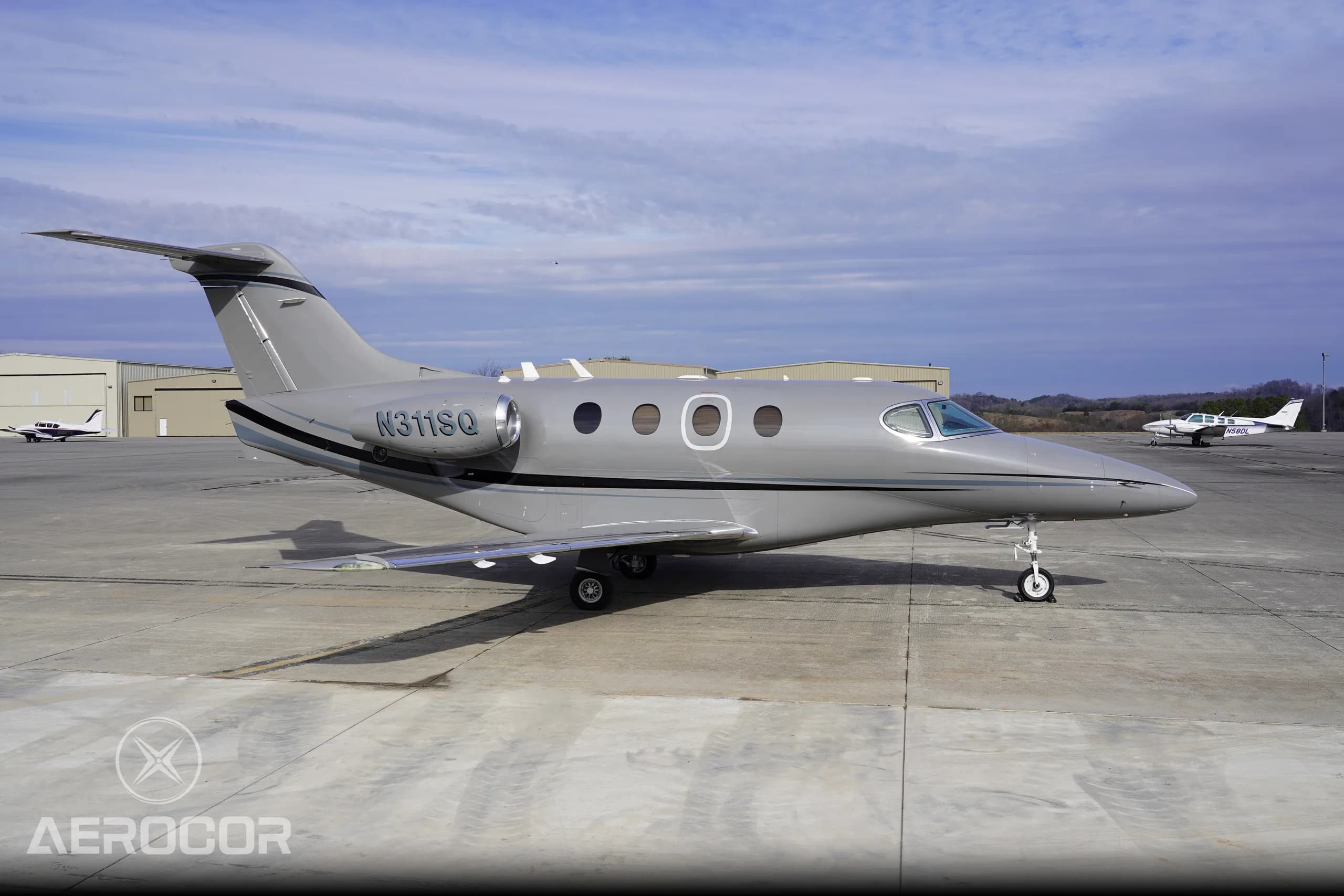 A side view of the gray Raytheon Premier I business jet, registration N311SQ, parked on an airport ramp with hangars in the background.