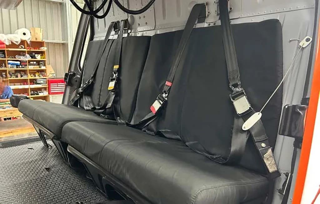 Three black passenger seats with seatbelts visible inside the cabin of a helicopter.