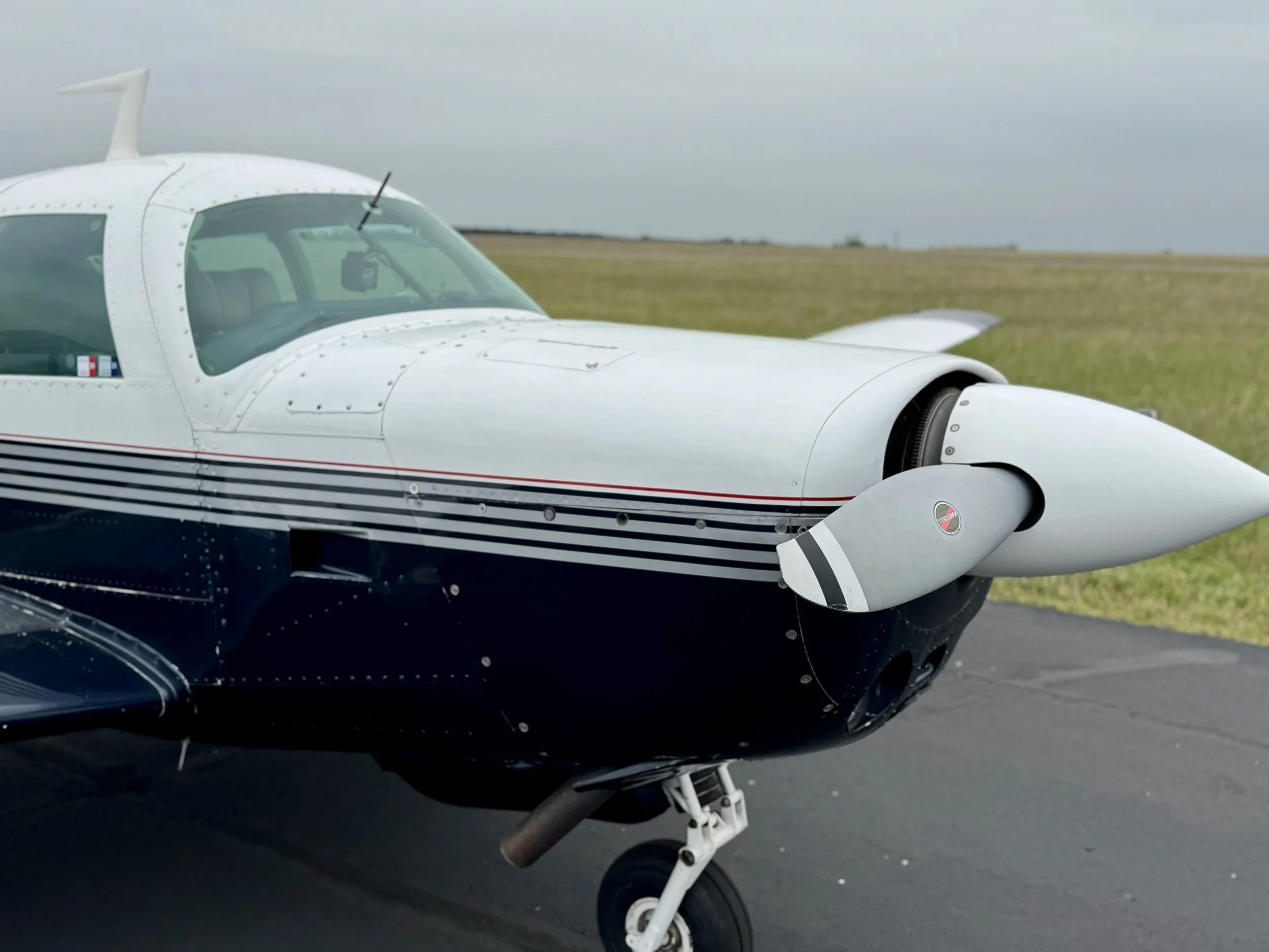 Close-up of the propeller and nose of a Beechcraft Bonanza aircraft with a white and blue paint scheme.