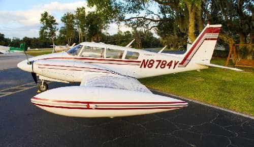 A white and red Piper aircraft, registration N8784Y, parked on the tarmac.