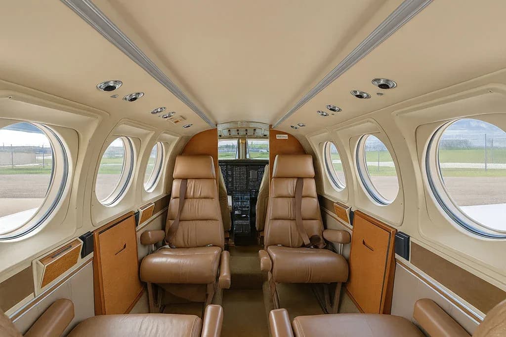 The aircraft cabin features tan leather seats arranged in a club configuration, with a view towards the cockpit.