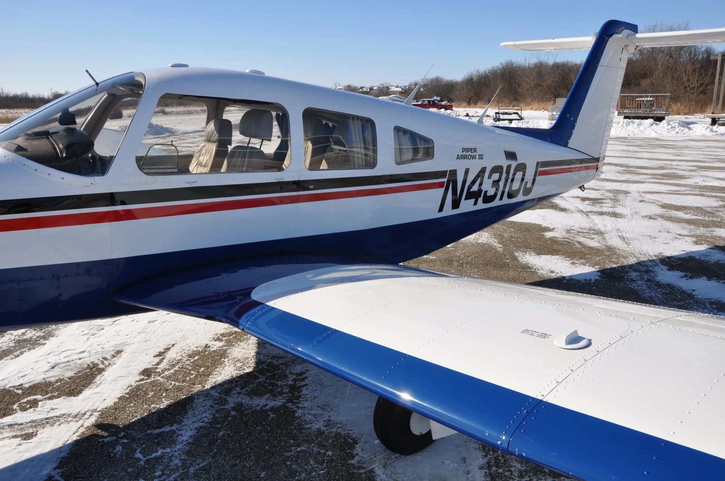 A close-up view of the rear fuselage, tail, and right wing of the Piper Arrow IV aircraft N4310J on a snowy tarmac.