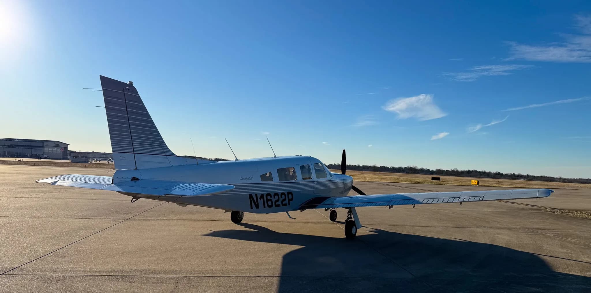 A rear three-quarter view of a white Piper Saratoga SP (N1622P) with grey stripes on an airfield at sunset.