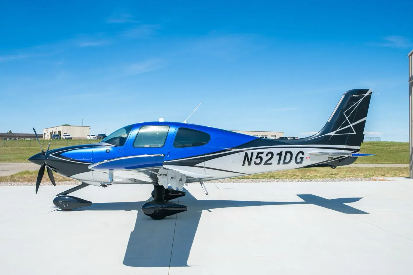 A blue, black, and white Cirrus SR22T aircraft with registration N521DG parked on a tarmac under a clear blue sky.