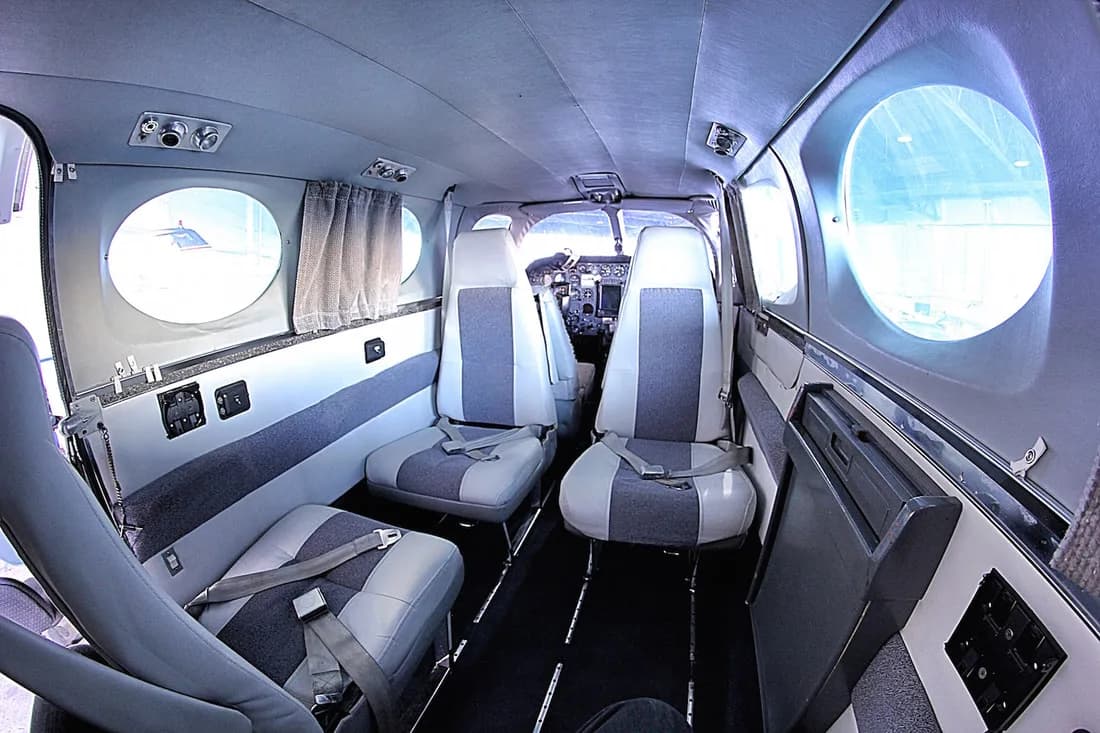 Aircraft interior with gray and white seats and round windows.