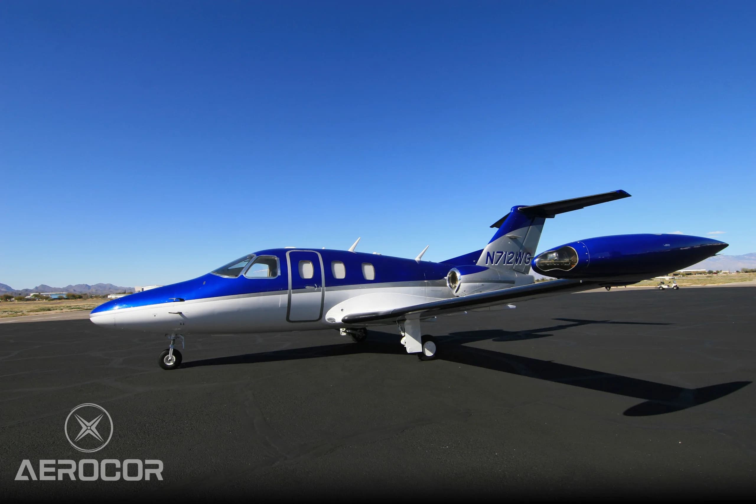 A side view of the blue and white Eclipse 500/550 jet, N712WG, parked on an airport tarmac.