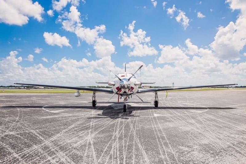 Front view of a Piper Meridian aircraft parked on the tarmac under a partly cloudy sky.
