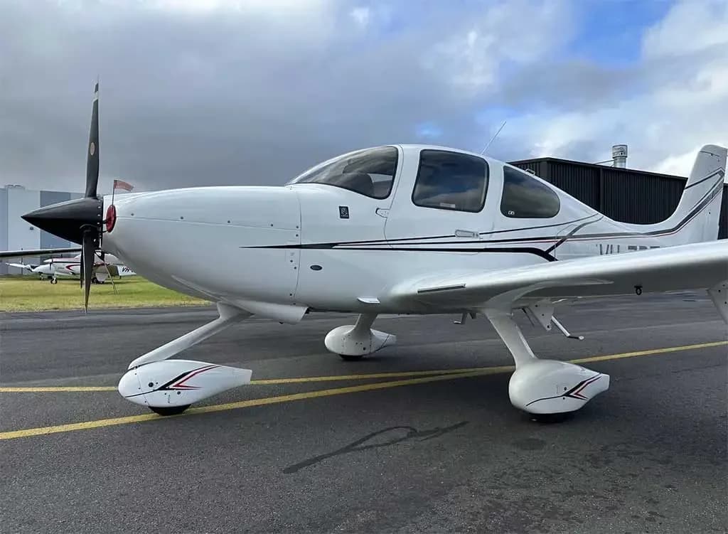 A front-side view of a white Cirrus SR22 aircraft with black and red stripes, registration VH-ZPZ, parked on a tarmac.