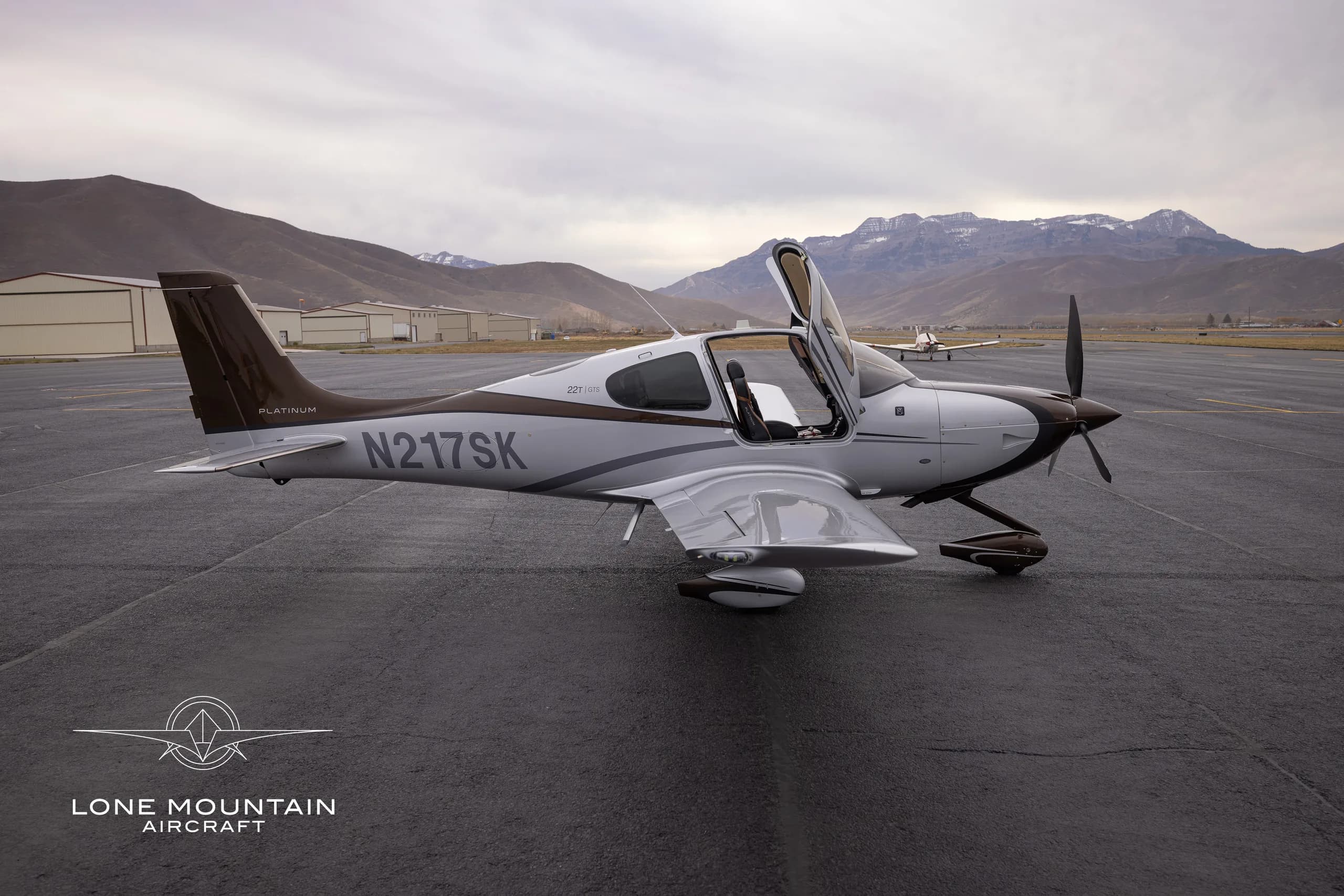 A Cirrus SR22T aircraft with a brown and white paint scheme is parked on the tarmac with the doors open.