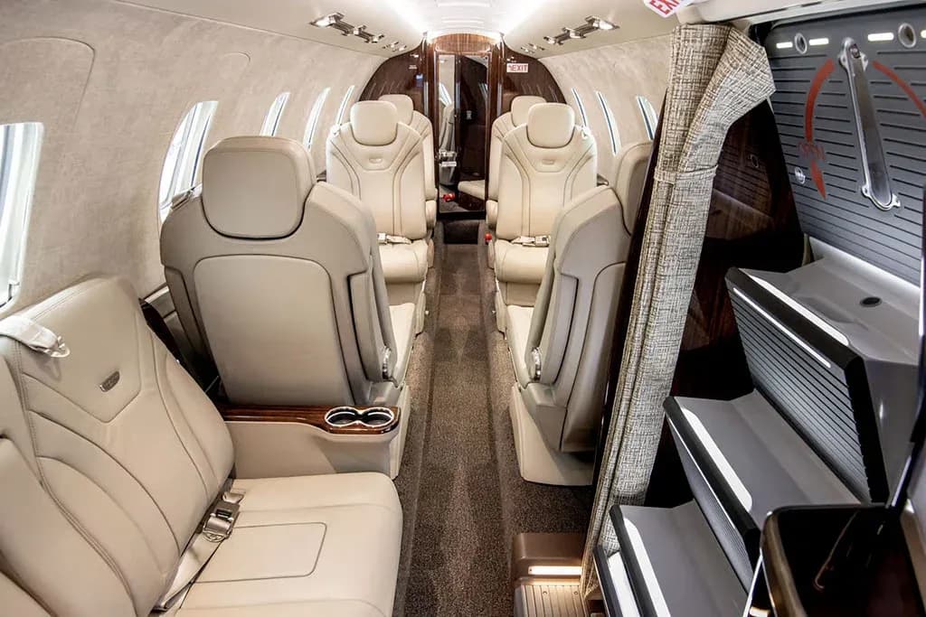 The luxurious interior cabin of a private jet features light tan leather seats and a view of the entry stairs and galley area.