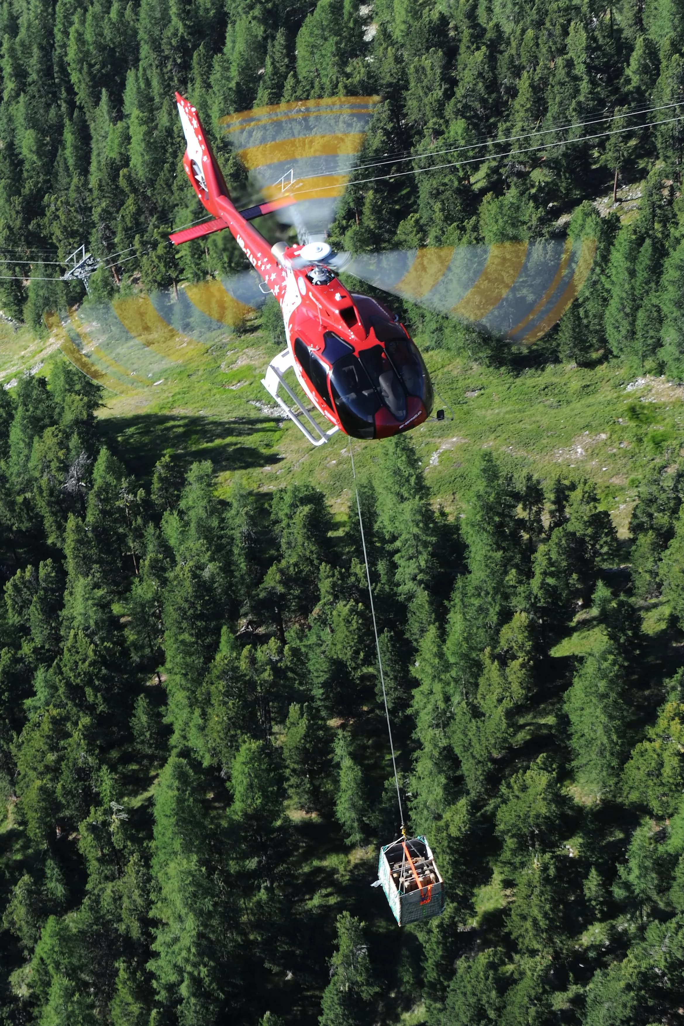 Red and white helicopter lifting a container over a forest.