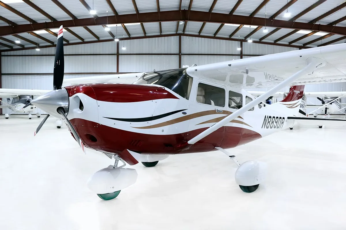 A front-side view of a red and white Cessna Stationair TC aircraft (N889DR) with gold accents, parked in a hangar.