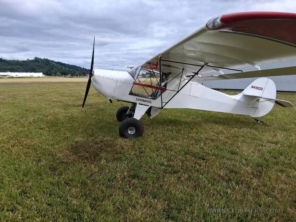 A white experimental aircraft with red accents on the wing and tail, registration N416DD, parked on a grassy field under a cloudy sky.