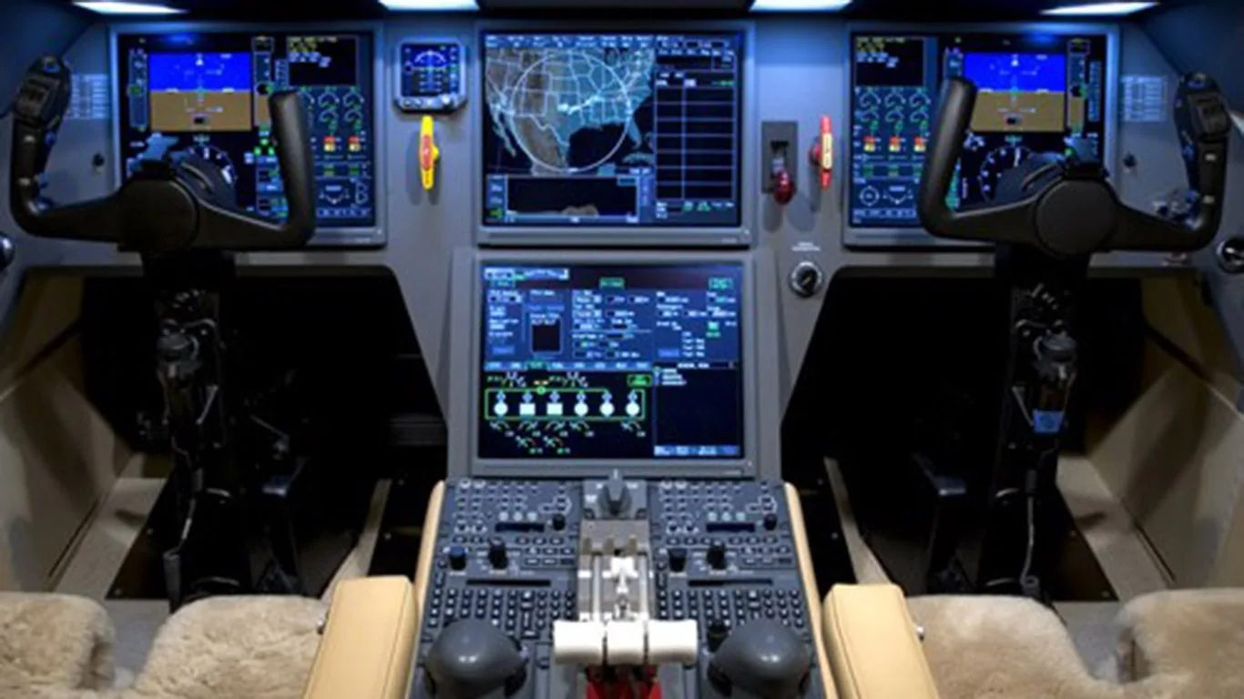 The modern cockpit of a business jet, featuring multiple large digital displays and control yokes.