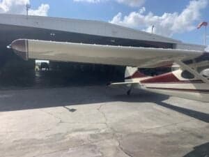 A Cessna 170A aircraft with a maroon and white paint scheme parked in front of a hangar.