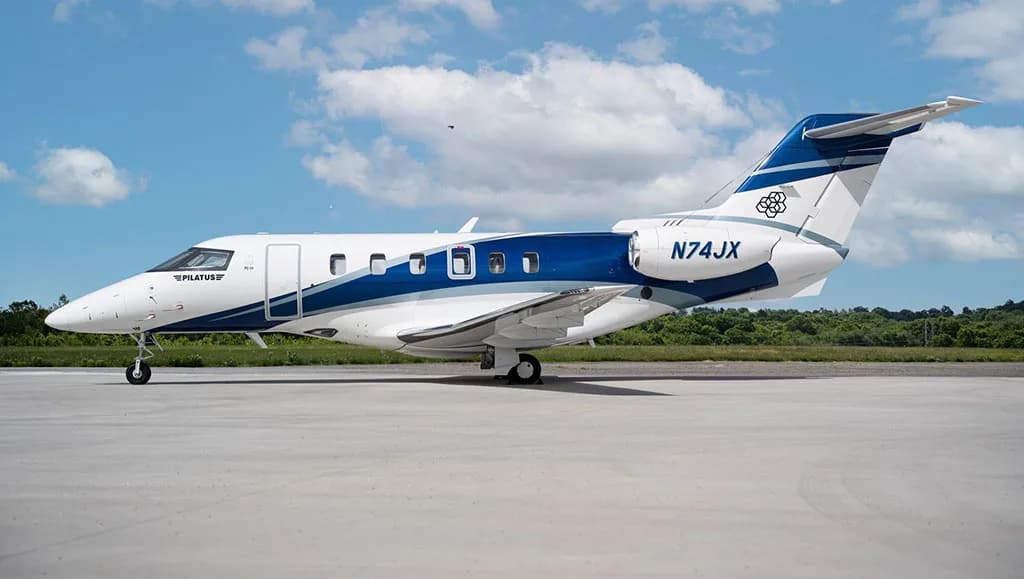 A Pilatus PC-24 business jet, registration N74JX, parked on an airfield under a partly cloudy sky.