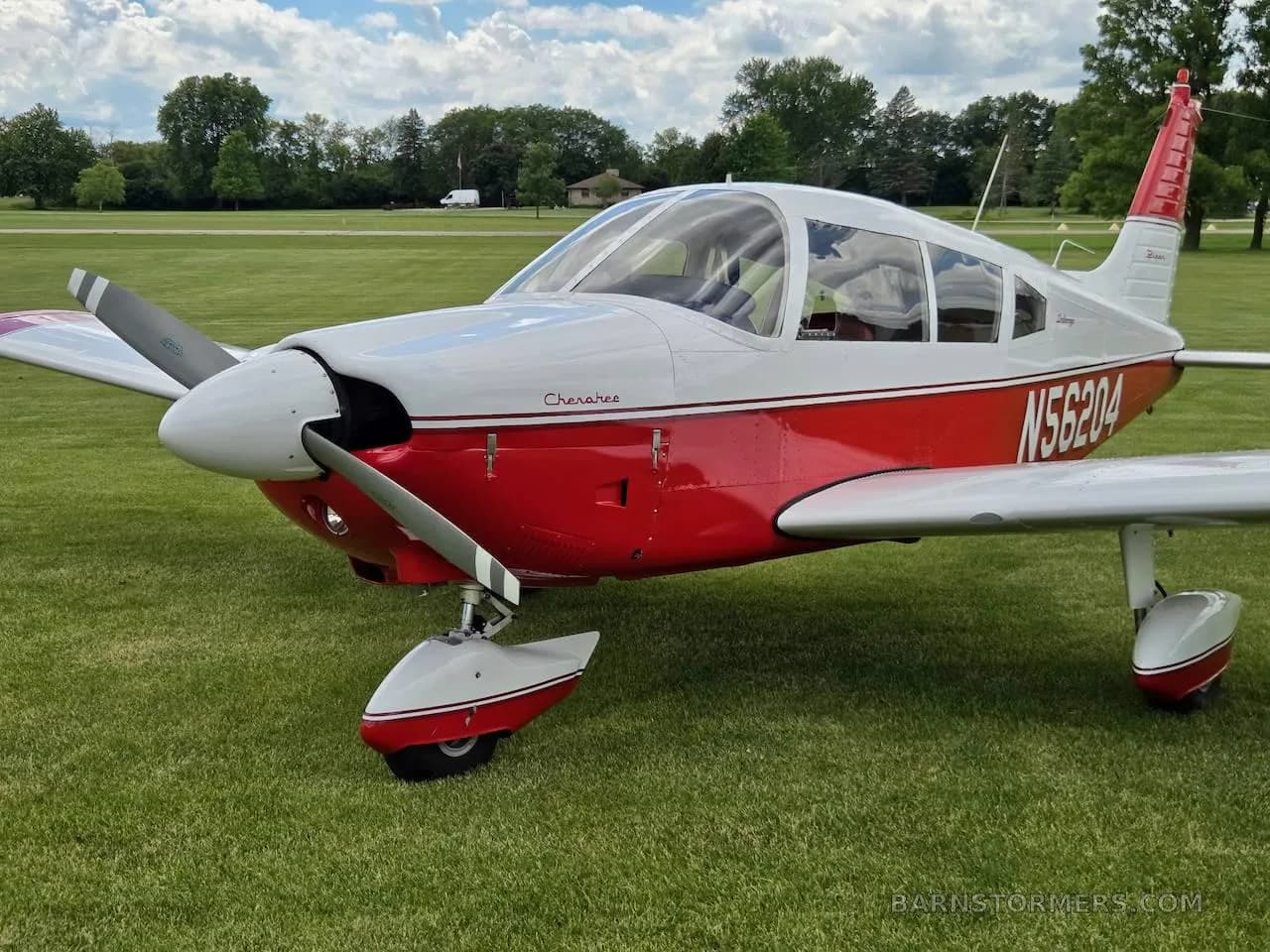 A close-up view of the front and side of a red and white Piper Cherokee aircraft (N56204) parked on grass.