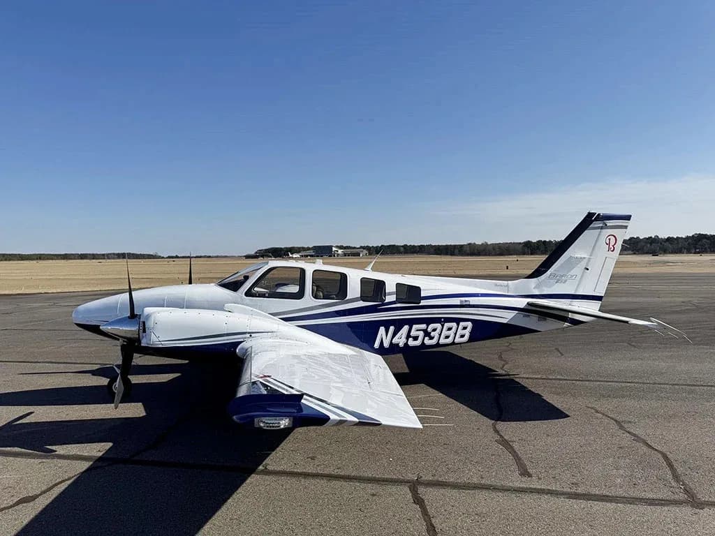 A white and blue Beechcraft Baron N453BB parked on an airfield, viewed from the front-right.