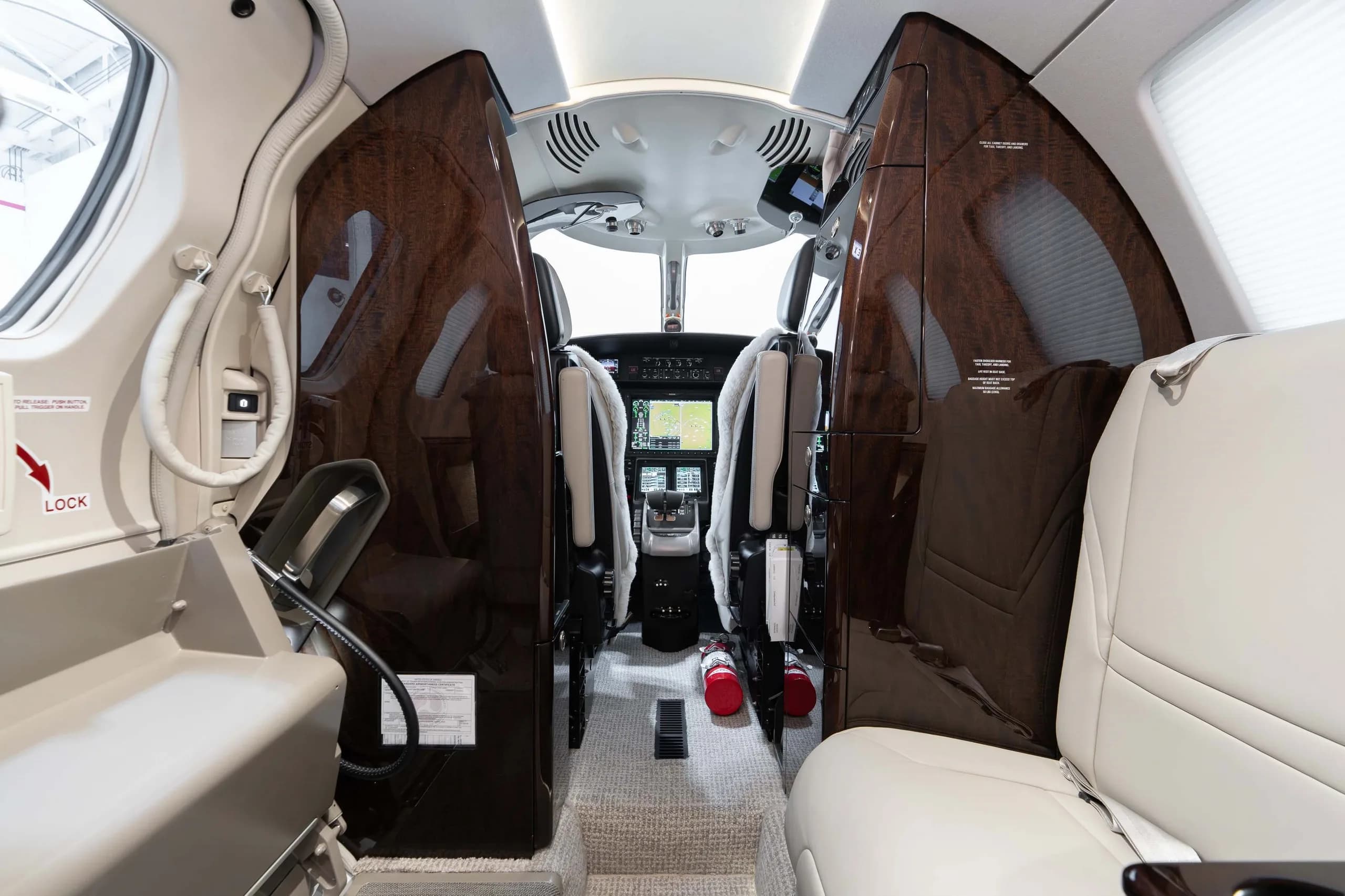 View from the business jet's cabin looking into the modern cockpit with two red fire extinguishers on the floor.