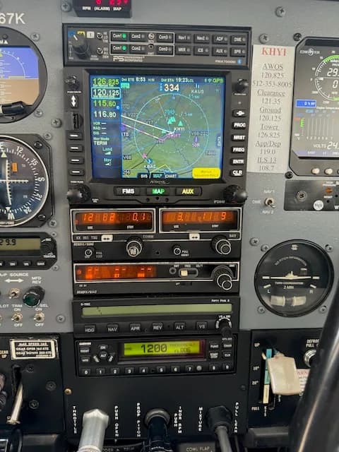 A close-up of the center stack of the Cessna 206 cockpit, displaying a GPS map and various radio and navigation controls.