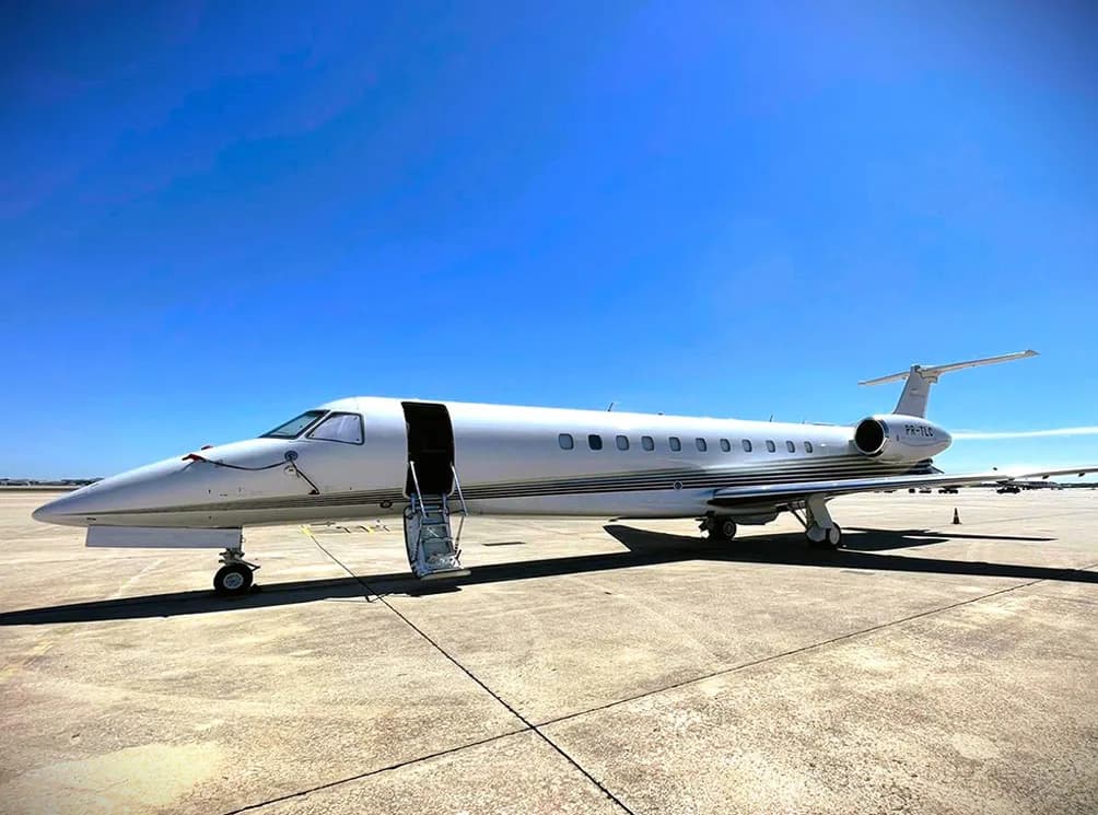 A white Embraer Legacy business jet parked on the tarmac with its door open and stairs deployed.