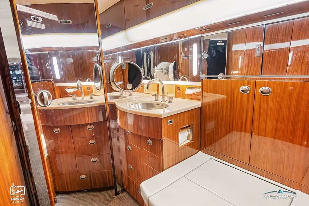 The aircraft lavatory with polished wood cabinetry, dual sinks, and large mirrors.