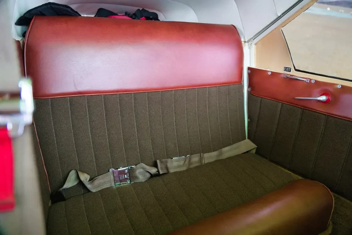 The brown and maroon rear seats of a small aircraft cabin with a visible seatbelt.