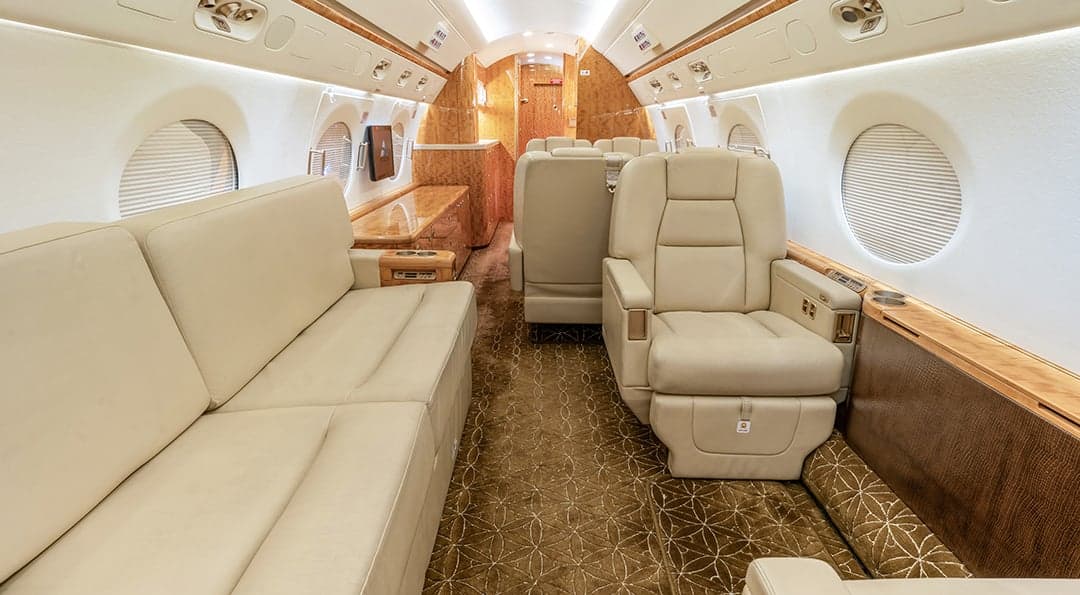The aircraft's interior features cream-colored leather seats and wood paneling.