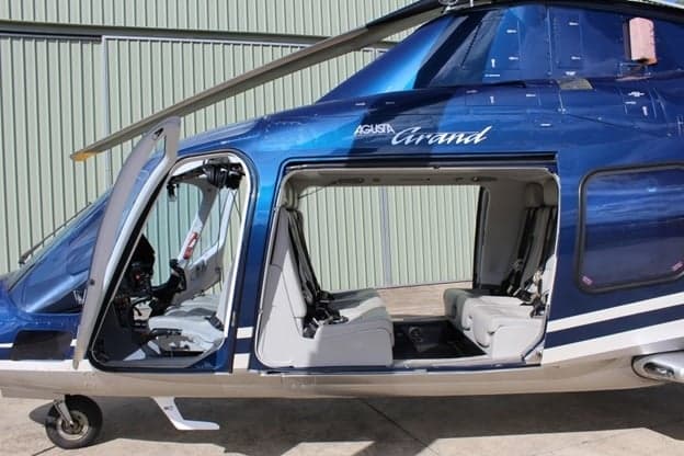 The interior of the Agusta Grand helicopter with the door open, showing the seats and cockpit.