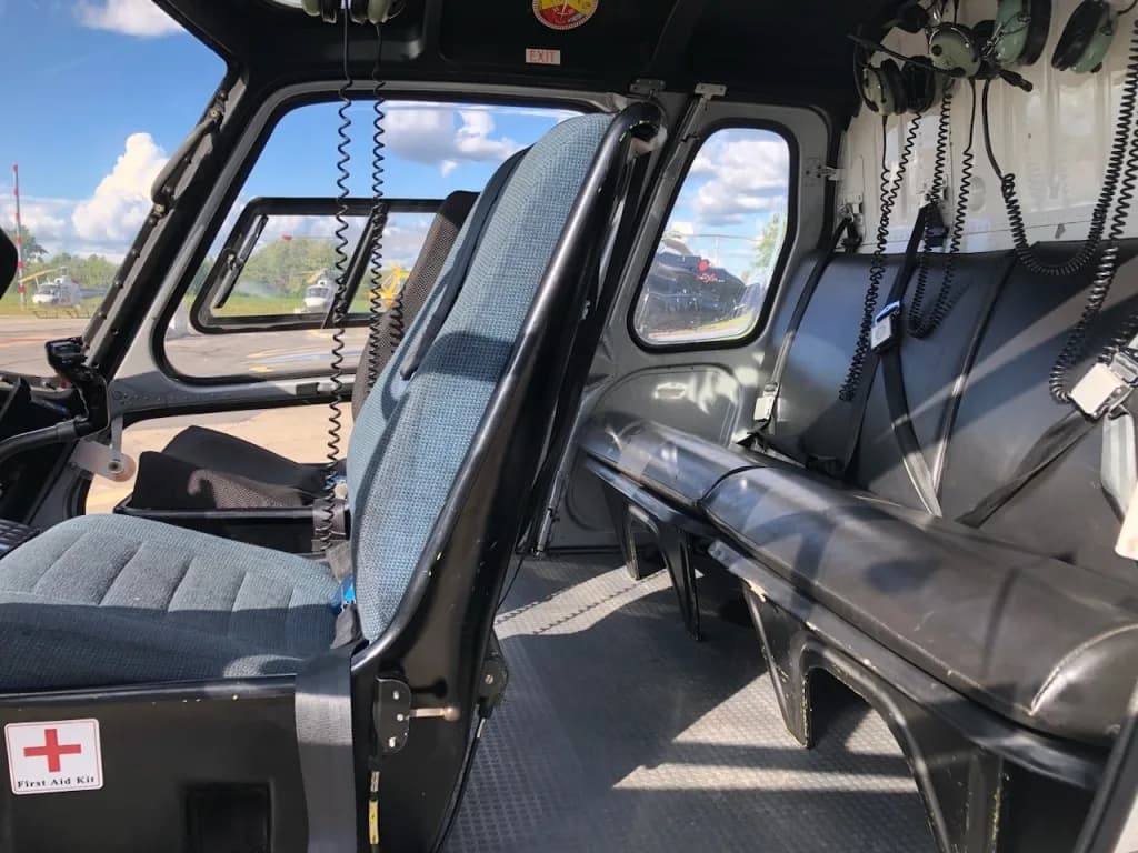 The interior cabin of a helicopter with blue fabric front seats and black leather rear bench seats, seen from the cockpit looking back.