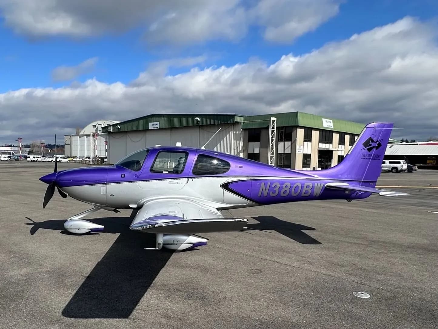 A purple and silver Cirrus SR22 aircraft, N380BW, parked on an airport tarmac under a partly cloudy sky.