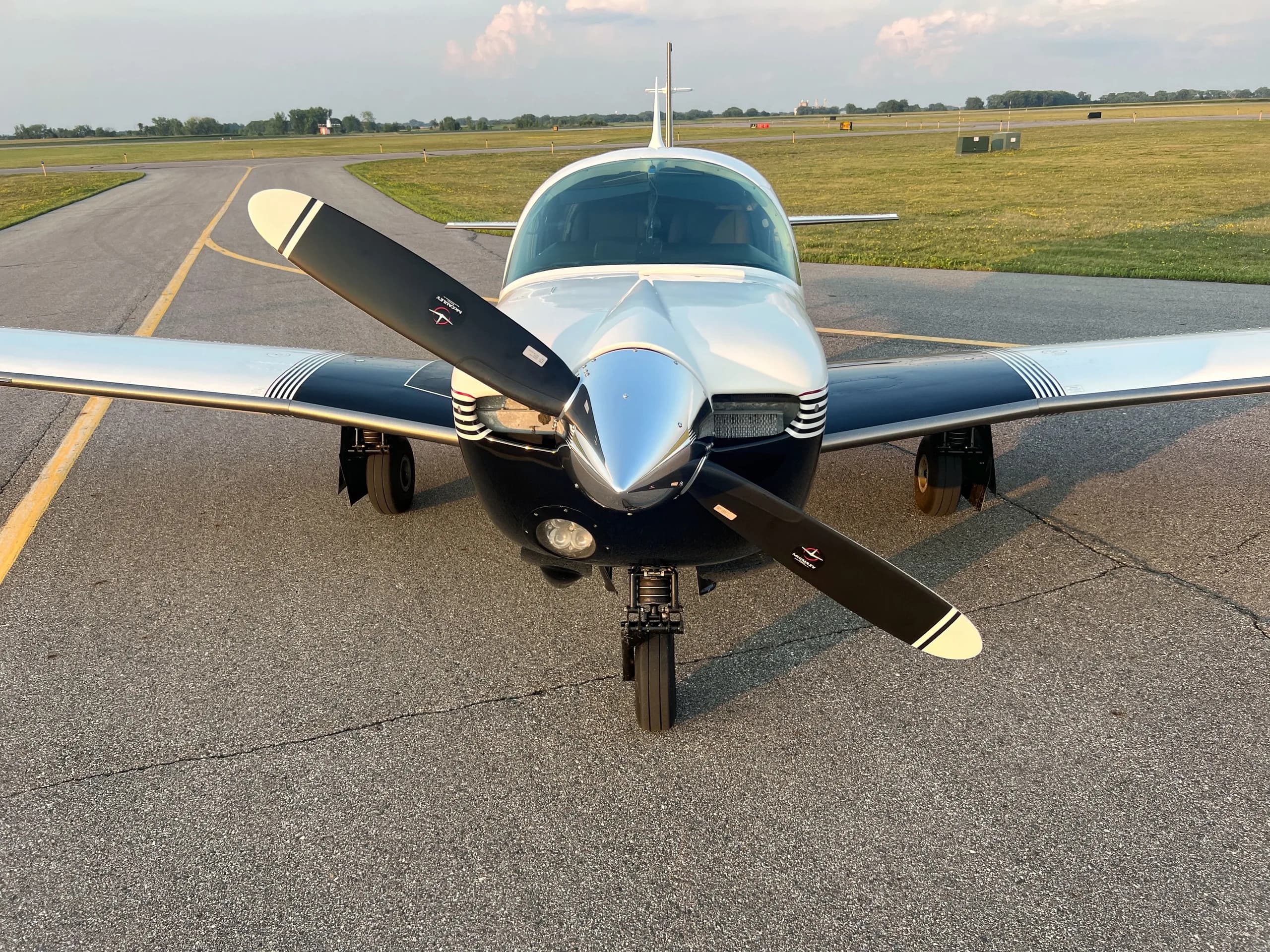 A head-on view of a white and dark blue single-engine aircraft with a two-bladed propeller on an airfield.