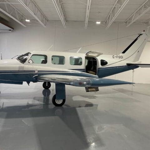 A Piper PA-31 Navajo is parked in a hangar with its door open.