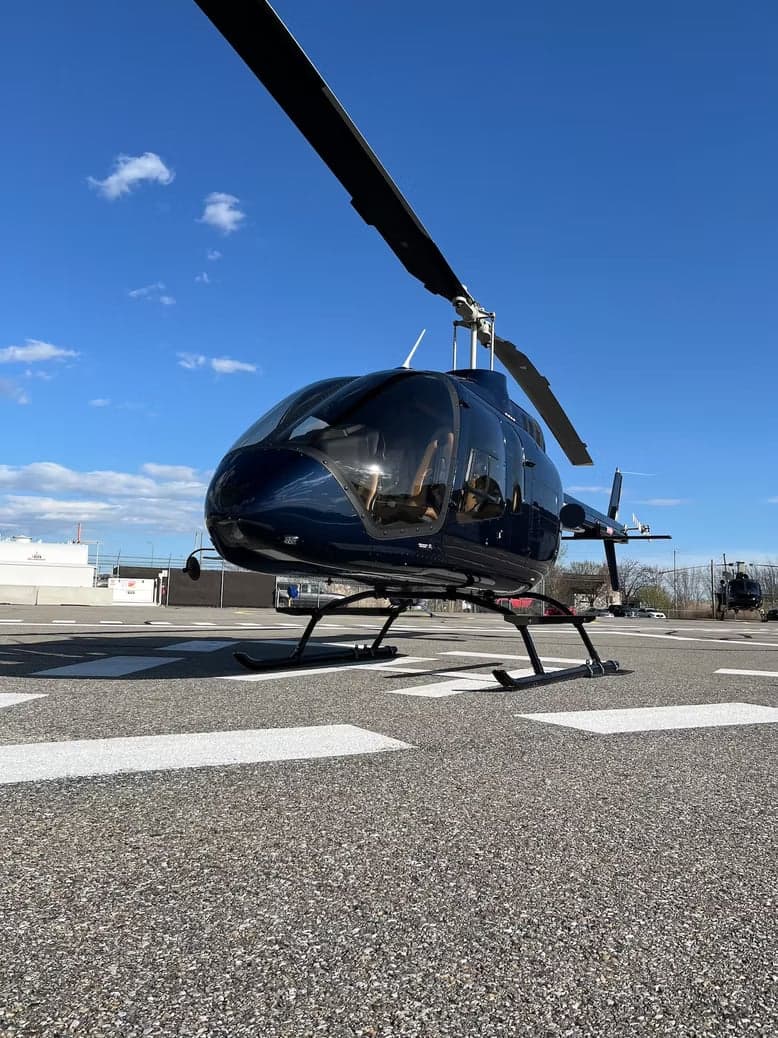 A dark blue Bell 505 helicopter is parked on the tarmac.