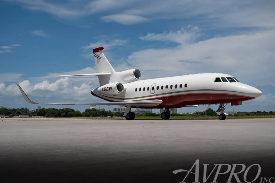 A Dassault Falcon 900EX business jet with a white and red paint scheme on the tarmac on a sunny day.