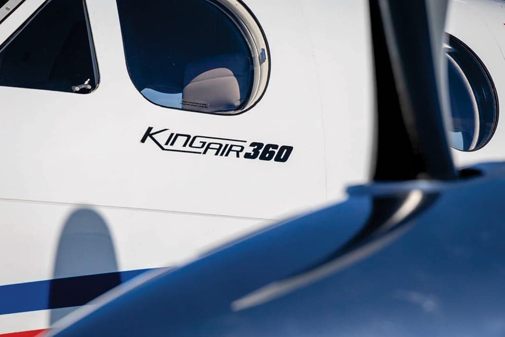 Close-up of the fuselage of a white King Air 360, showing the "KINGAIR 360" text and blue and red stripes.