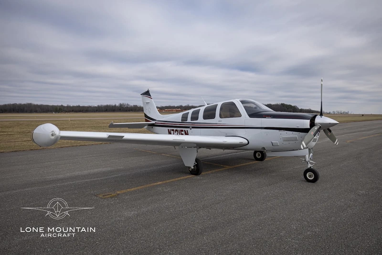 A three-quarter front view of the N721EN single-engine propeller aircraft, showing its white, black, and red paint scheme on an airfield.