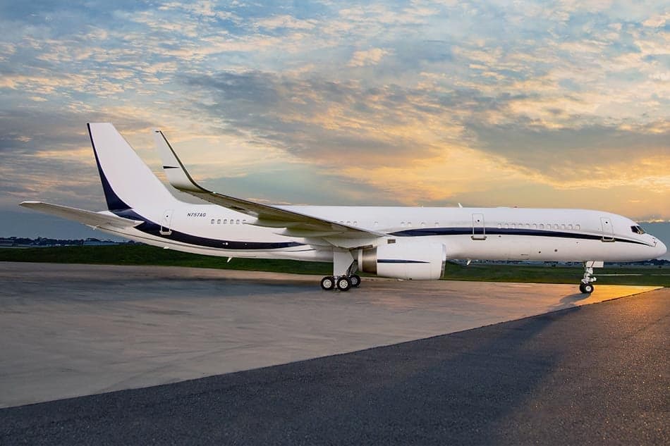 A white and navy Boeing 757 business jet is parked on the tarmac at sunset.
